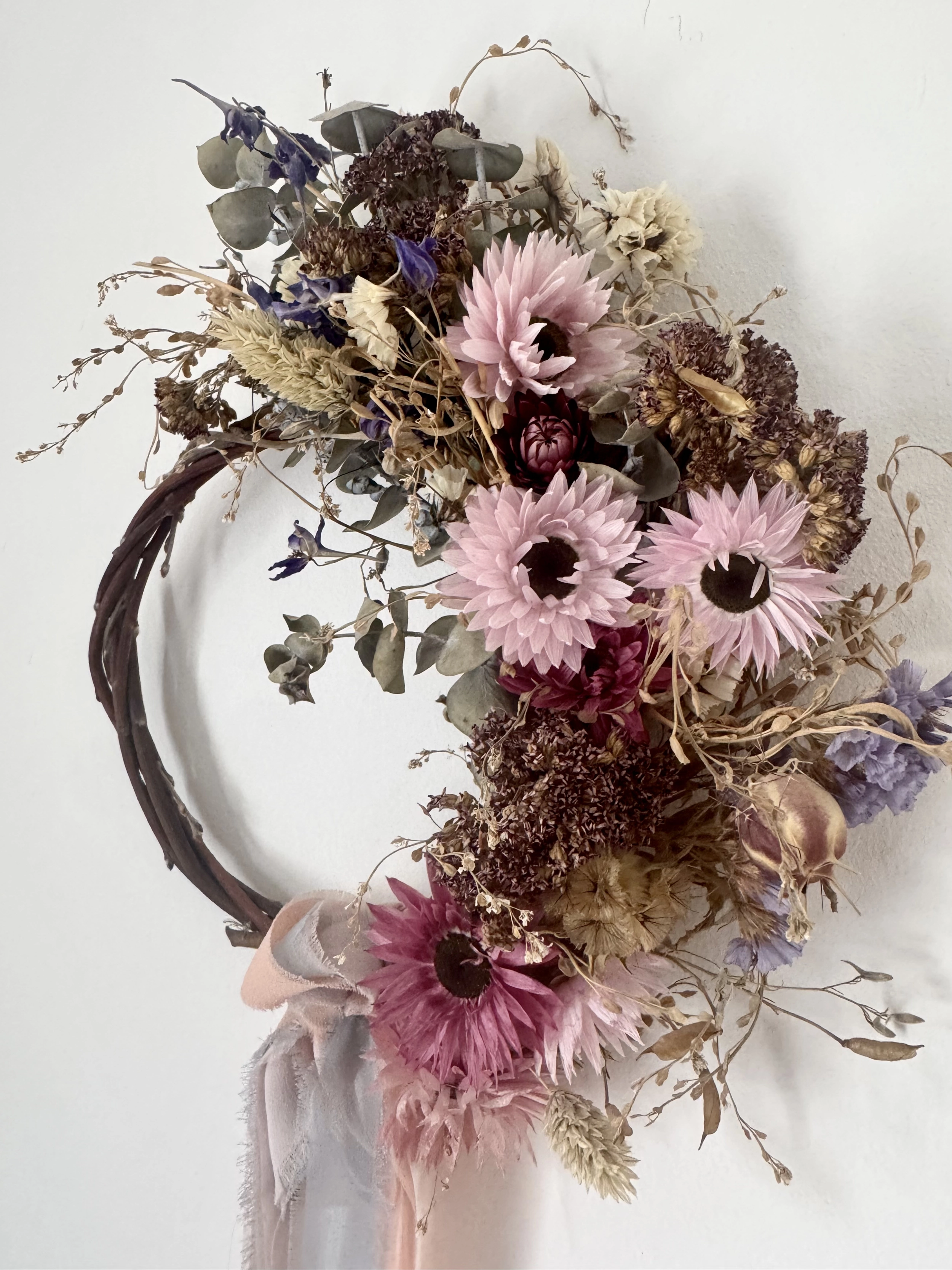 A willow wreath filled with dried pink, burgundy and natural flowers
