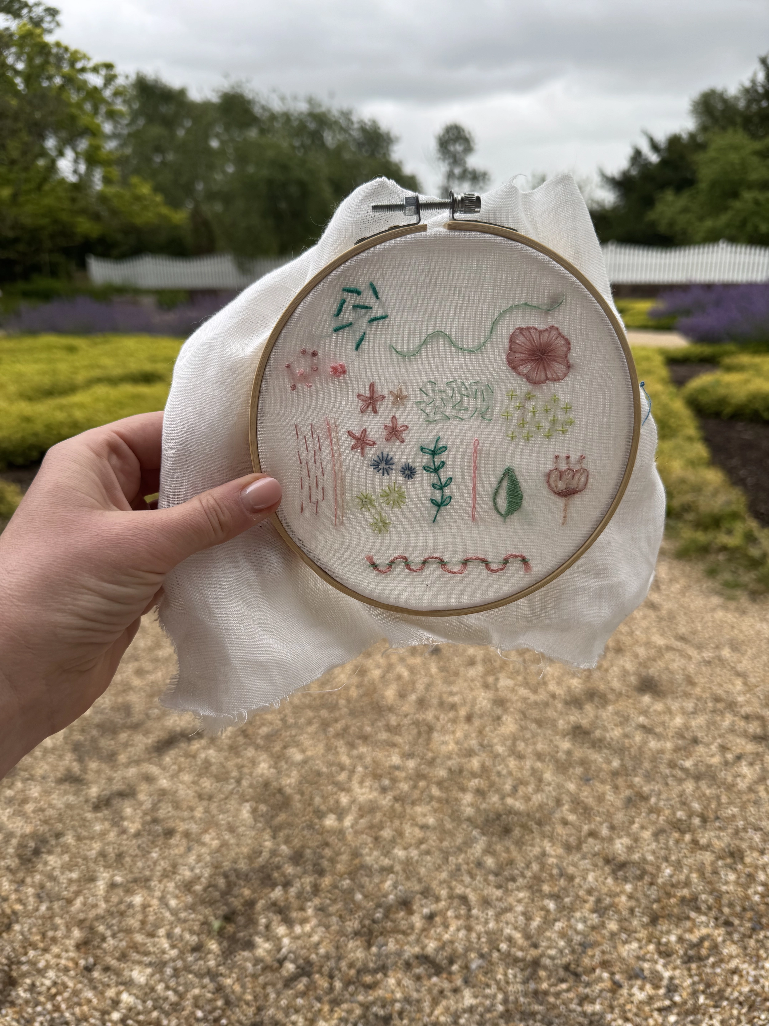 A floral embroidery sampler in a wooden hoop, held in a garden