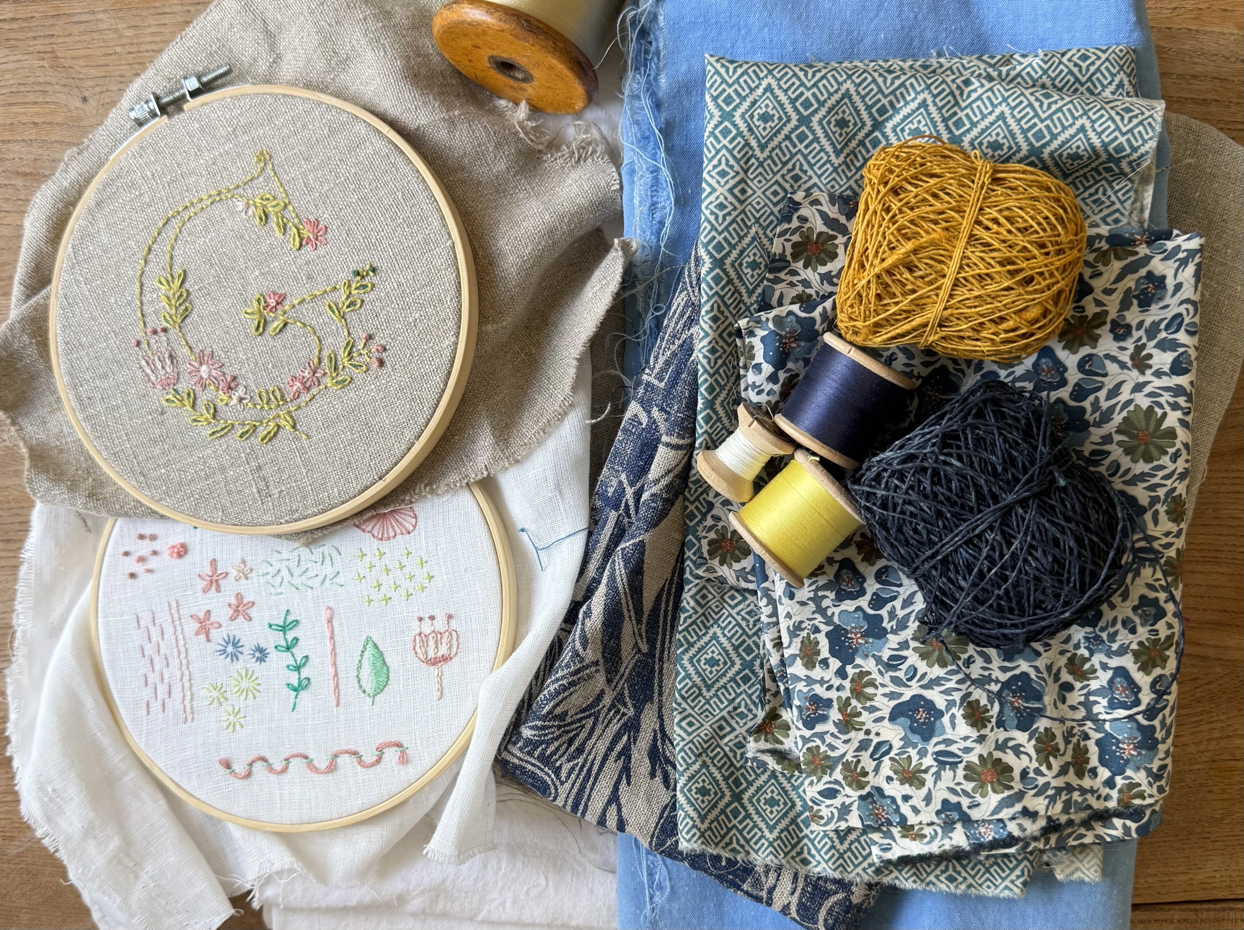 Embroidery hoops, patterned cloth, thread spools and yarn arranged on a wooden making table