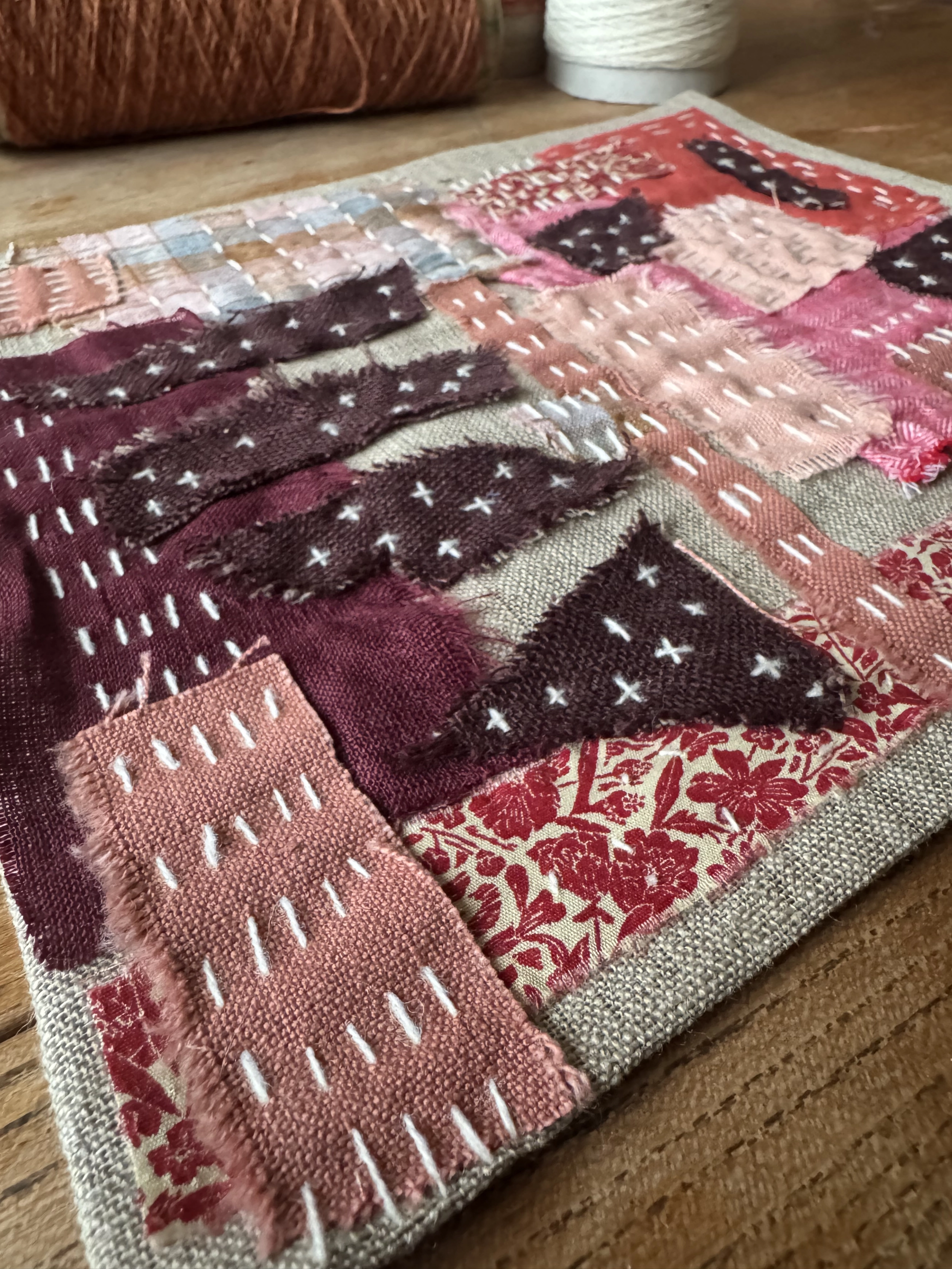 Close-up of a hand-stitched fabric collage in red, pink and plum